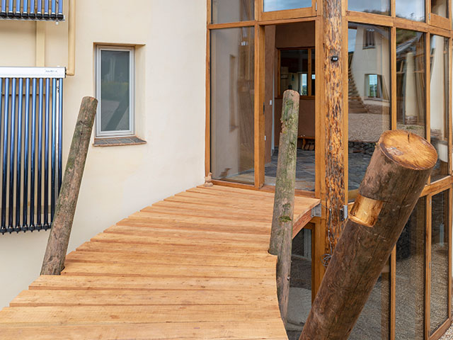 Wooden drawbridge pathway leading to main entrance with wooden archway of Grand Designs cob house