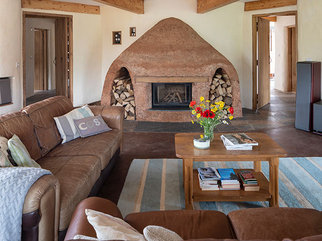 Cob fireplace with brown leather sofa, wooden coffee table decorated with vibrant bouquet and blue striped rug