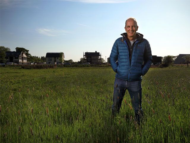 Kevin McCloud standing in a field in front of houses featured on Grand Designs: The Street -kevin-mccloud-granddesignsmagazine.com