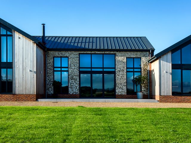 A prefab barn conversion with stone walls and corrugated metal roof in Norfolk by Swann Edwards Architecture