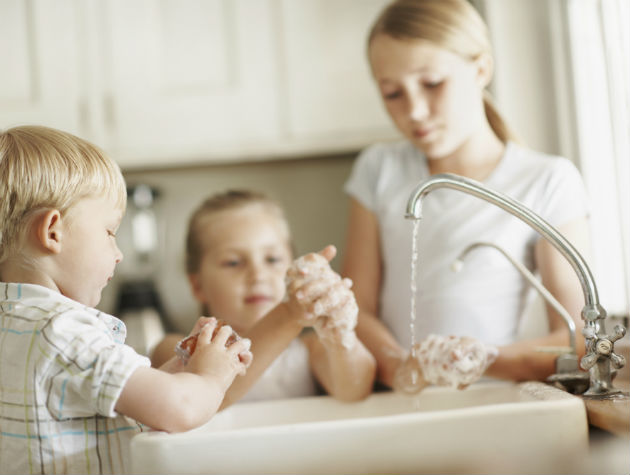 three children in a kitchen washing hands under a running tap