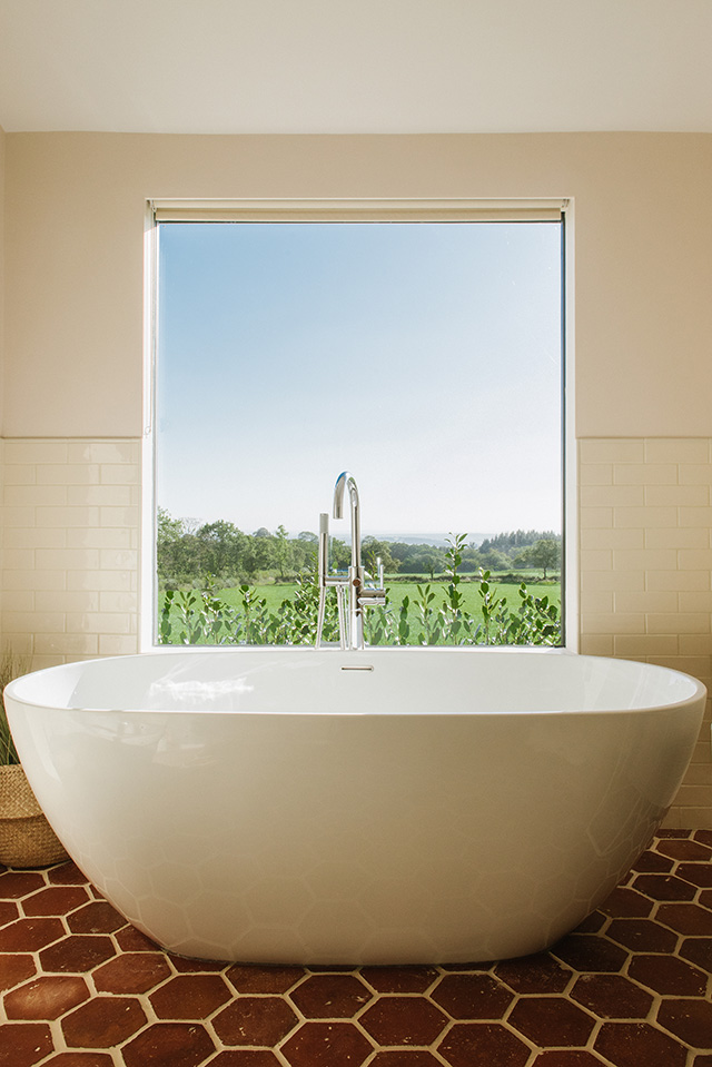 Bathroom with terracotta tiles, modern bath and large picture window - self-build homes - grand designs