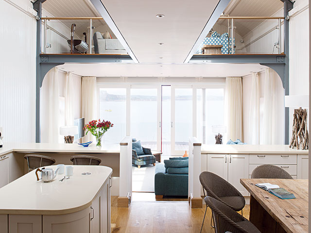 Kitchen space with island and dining table, looking up to clear gallow hallway