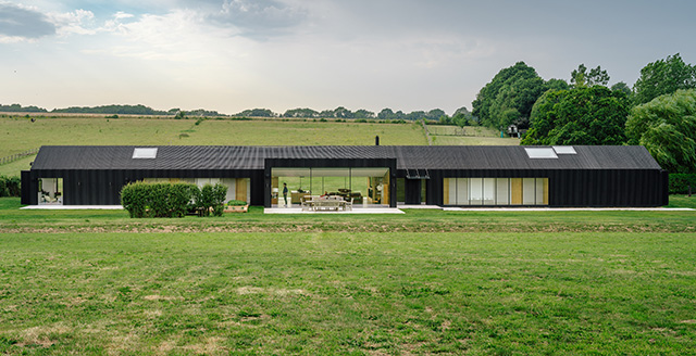 A long, low house seen from the exterior with dark timber cladding 