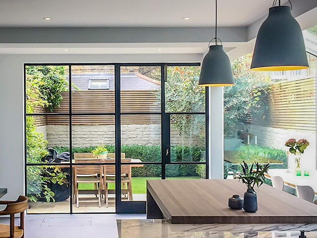 Open-plan dining area with panels of metal-frame glazing giving a view out onto a small courtyard garden