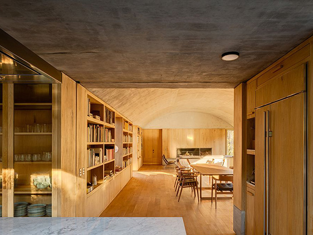 View from the kitchen to the dining area with timber floors, concrete ceiling and built-in wooden furniture