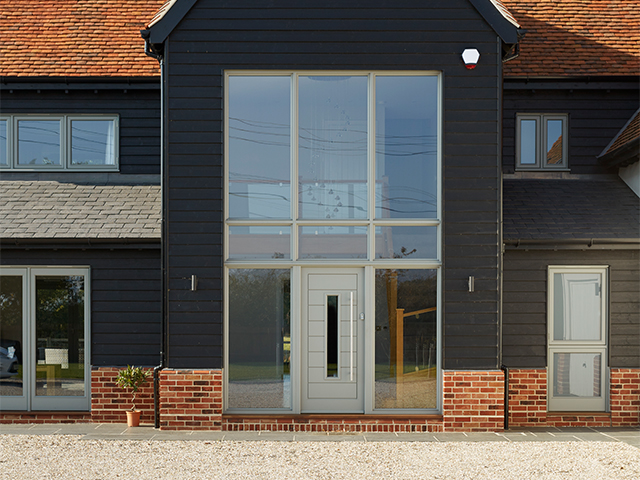 Front exterior of a barn conversion with a grey front door and glazed side panels.