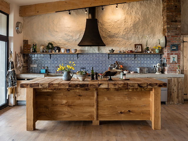 An island made from railway sleepers stands in front of a run of timber cabinets with concrete worksurface