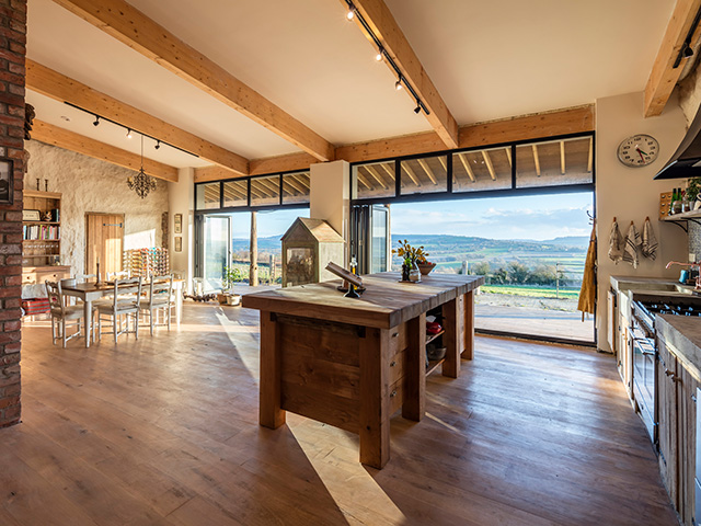 A view of the kitchen with the bi-folding doors open to the terrace and countryside beyond