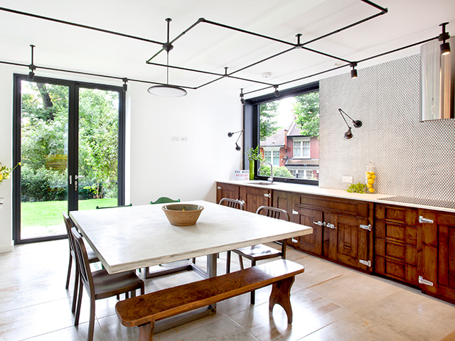 A big square table at the centre of a kitchen where base units run along one wall. Grand Designs kitchens