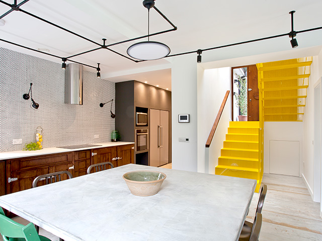 A view across the dining table towards the hall and stairs. The laser cut metal staircase is bright yellow.