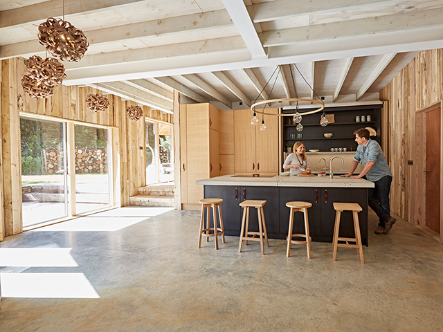 Danie and Tom Raffield stand at the island in their timber-clad kitchen with oak veneer cabinets