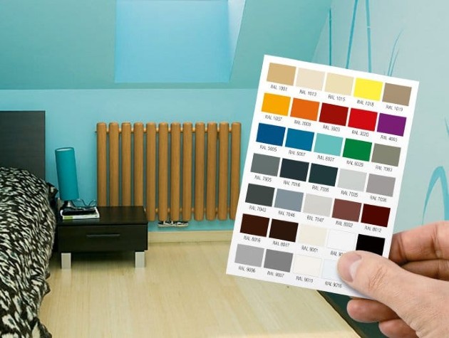 hand holding colour chart in room with blue walls bed and radiator