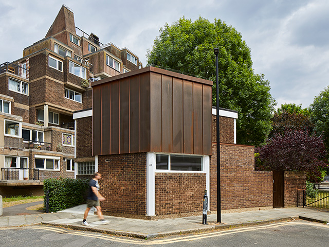 Exterior of the brick and concrete Brutalist house on a London street. The copper clad extension is on the second floor.