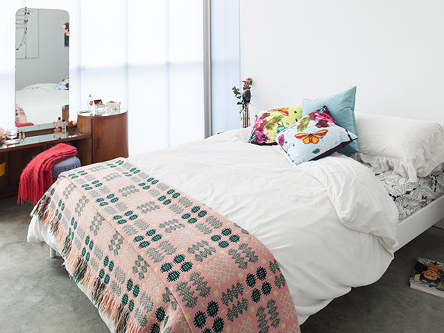 Double bed with pink tartan blanket, white bedding and colourful cushions. An artisan dressing table with large portrait mirror stands adjacent