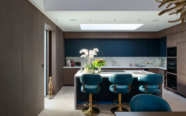 Dark blue and wood cabinets in the fitted kitchen with island unit and bar chairs in the Grand Designs graveyard house