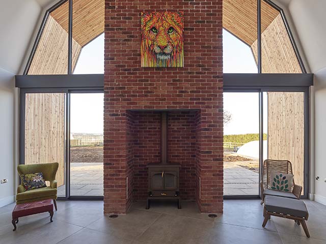 A woodburning stove with brickwork chimney fireplace in a the Grand Designs Dutch barn in Lincolnshire