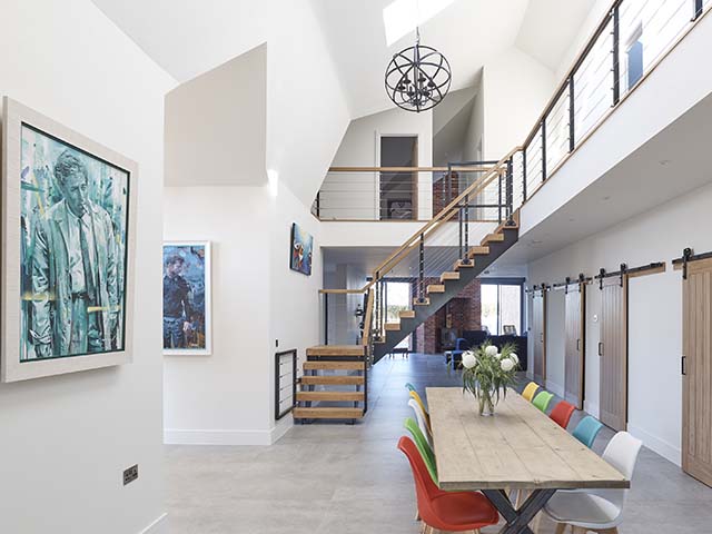 An open plan living space in a modern barn with wooden table, colourful plastic chairs and open staircase 