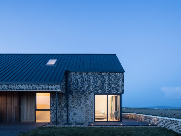 remote landscape with a flint clad steel roof house with panoramic glazing