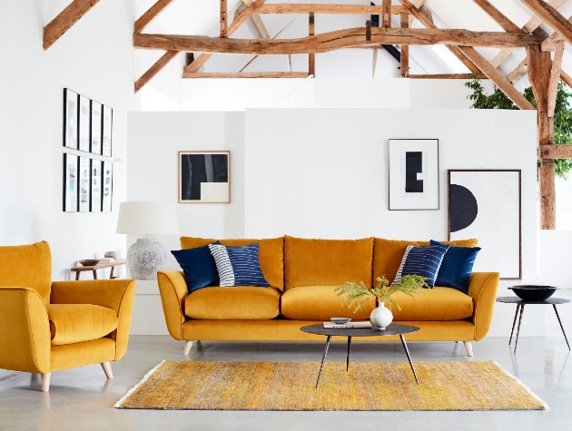 Mid Century style mustard velvet sofa with blue cushions in a white barn interior with exposed beams