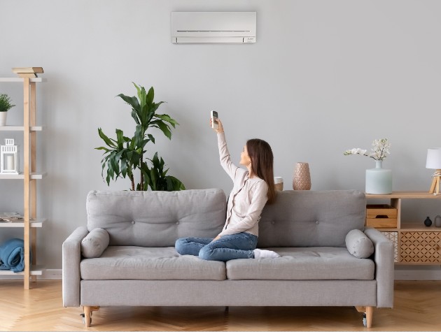 neutral living room with woman on grey modern sofa operating wall mounted air conditioning unit