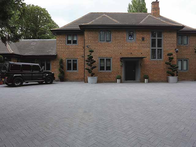 A large expanse of paving arranged in a herringbone pattern in front of a red brick house. A good choice of driveway material for this particular setting.