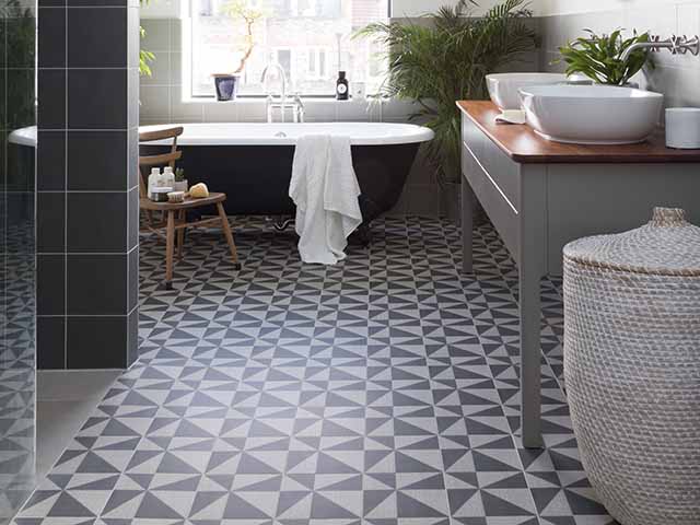 Large loft bathroom with highly patterned floor and freestanding bath beneath the window