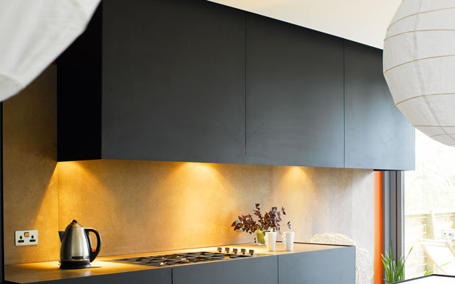 Dark grey handleless cabinets in the Grand Designs Brighton mansion kitchen. Downlighters illuminate the worksurface.