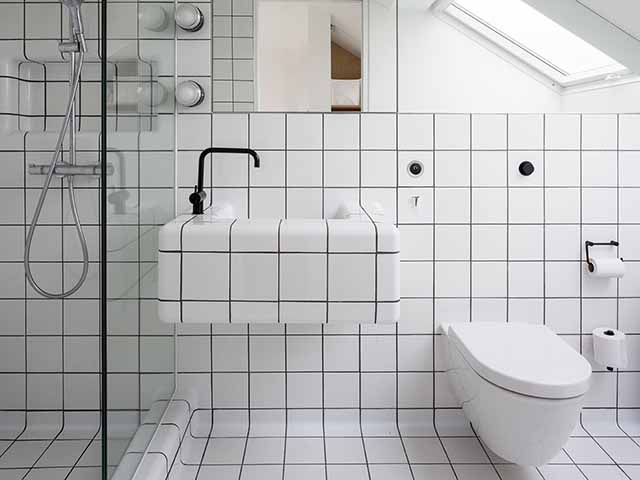 White tiled loft bathroom with sloping ceiling, walk-in shower, basin and loo