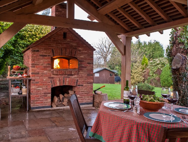 covered patio with table chairs and pizza oven