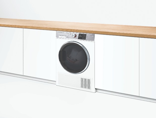 contemporary interior of white kitchen cabinets wooden worktop and white Fisher Paykel washing machine