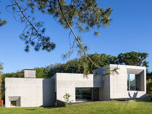 The exterior of the Grand Designs concrete house with trees, grass and a blue sky