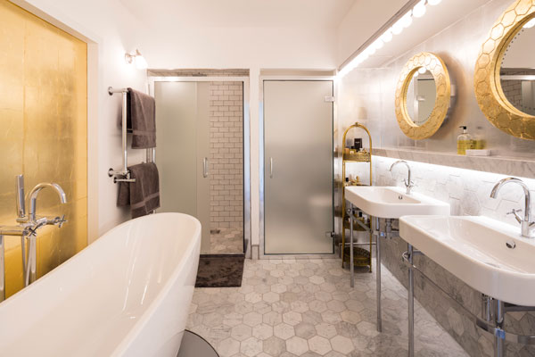 En suite bathroom with gold-leaf wall panel, gold mirrors and grey tiles 