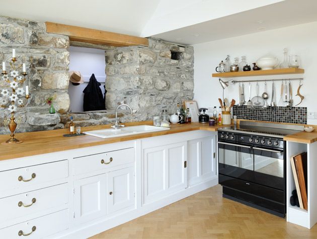 cottage kitchen with exposed stone walls, wooden worktops and white cabinets