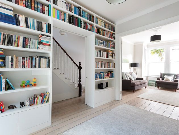 floor to ceiling bookcase purple sofa wooden flooring white rugs base of stairs