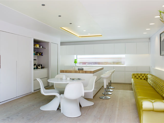 The basement kitchen is minimalist white with a colour-pop yellow sofa