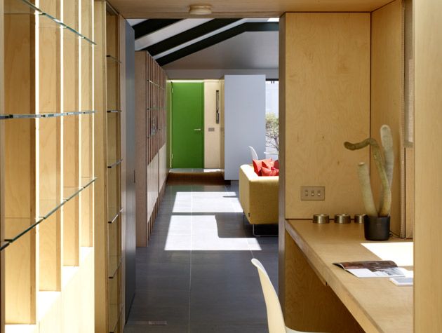wooden panelled hallway with desk area leading to open plan living room with yellow sofa and green front door