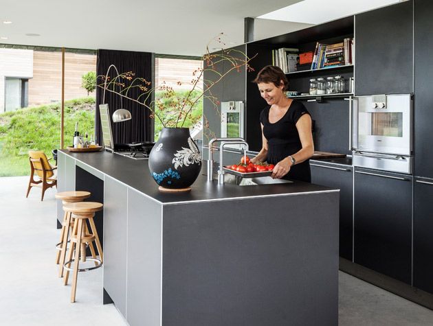 woman in black clothing cooking in contemporary kitchen  large black vase wooden barstools 