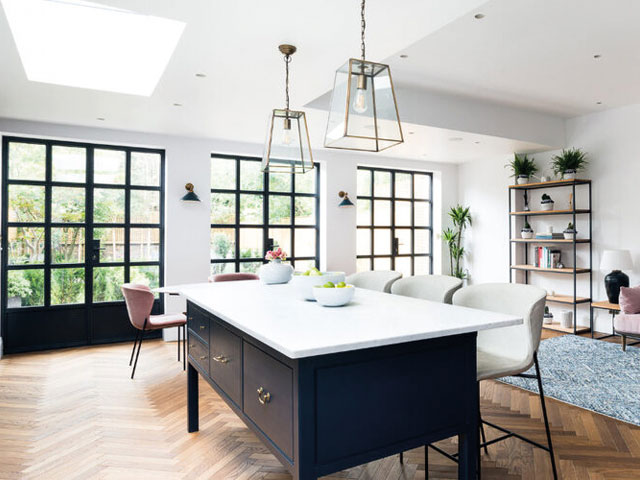 Crittall style doors in open plan kitchen dining area herringbone flooring raised blue kitchen island white barstools