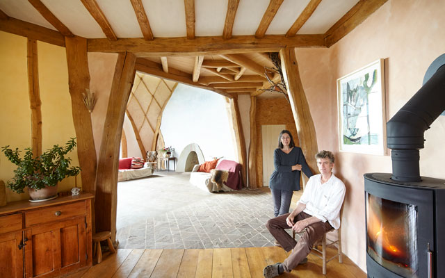 Ed and Rowena Waghorn in their timber frame Dug Out house from Grand Designs, relaxing by a woodburning stove 