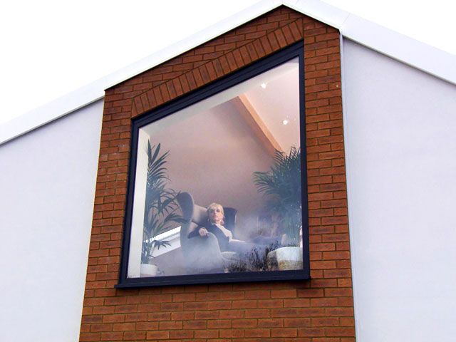 Sue sitting on a chair by the window in the glass house featured on Grand Designs The Street Episode 5 on Channel 4 