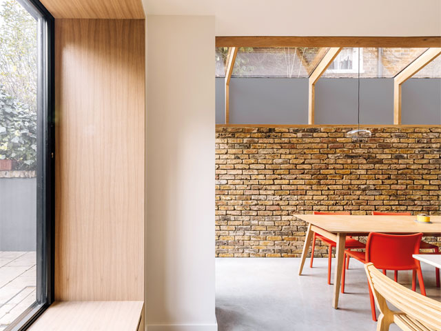 interior of exposed brick extension with large glazed window and dining table with red chairs