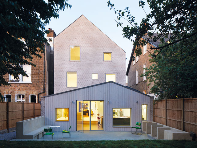 White timber and grey brick three storey home retrofit with outdoor seating area with green chairs 