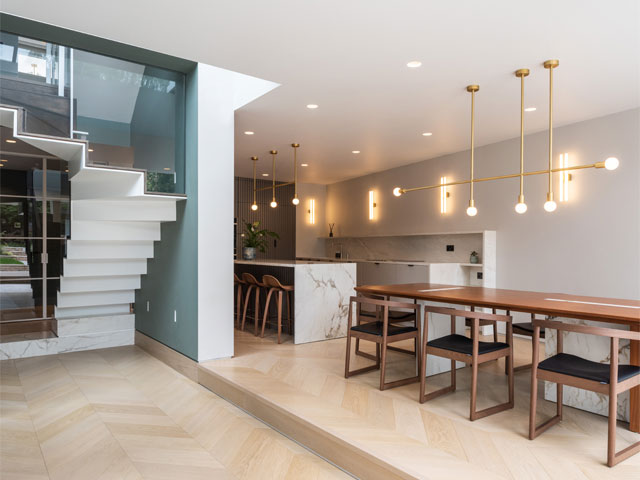 contemporary white staircase next to open plan kitchen dining room with gold light fixtures marble countertops herringbone wood flooring
