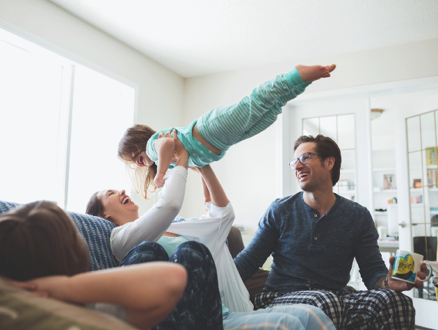 family on sofa in pyjamas youngest child being held aloft - home with stone wool insulation