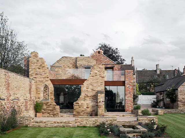 Rear exterior view of a Corten steel and glass extension nestled inside the ruined walls of an old factory