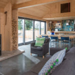 Looking through the open-plan living room of the Grand Designs modern barn house with grey sofa and woodburning stove