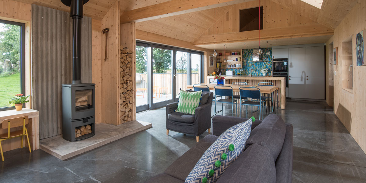 Looking through the open-plan living room of the Grand Designs modern barn house with grey sofa and woodburning stove