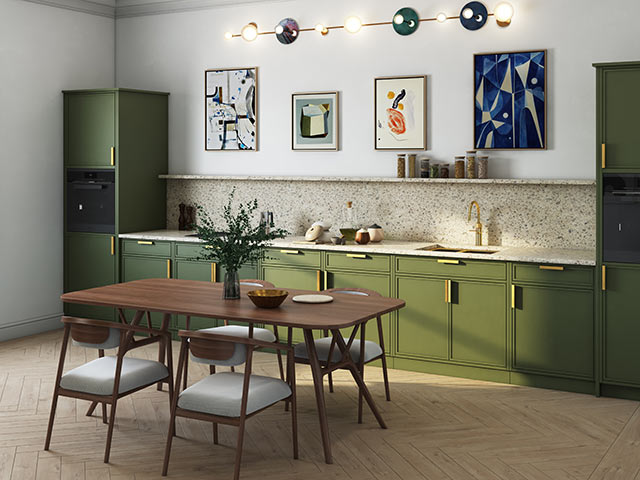 Dining area in kitchen diner space with green cupboards and brass handles