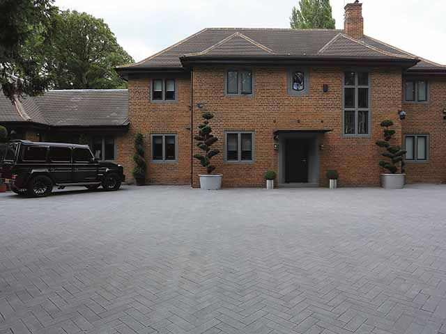 A large expanse of paving arranged in a herringbone pattern in front of a red brick house. A good choice for this particular setting.
